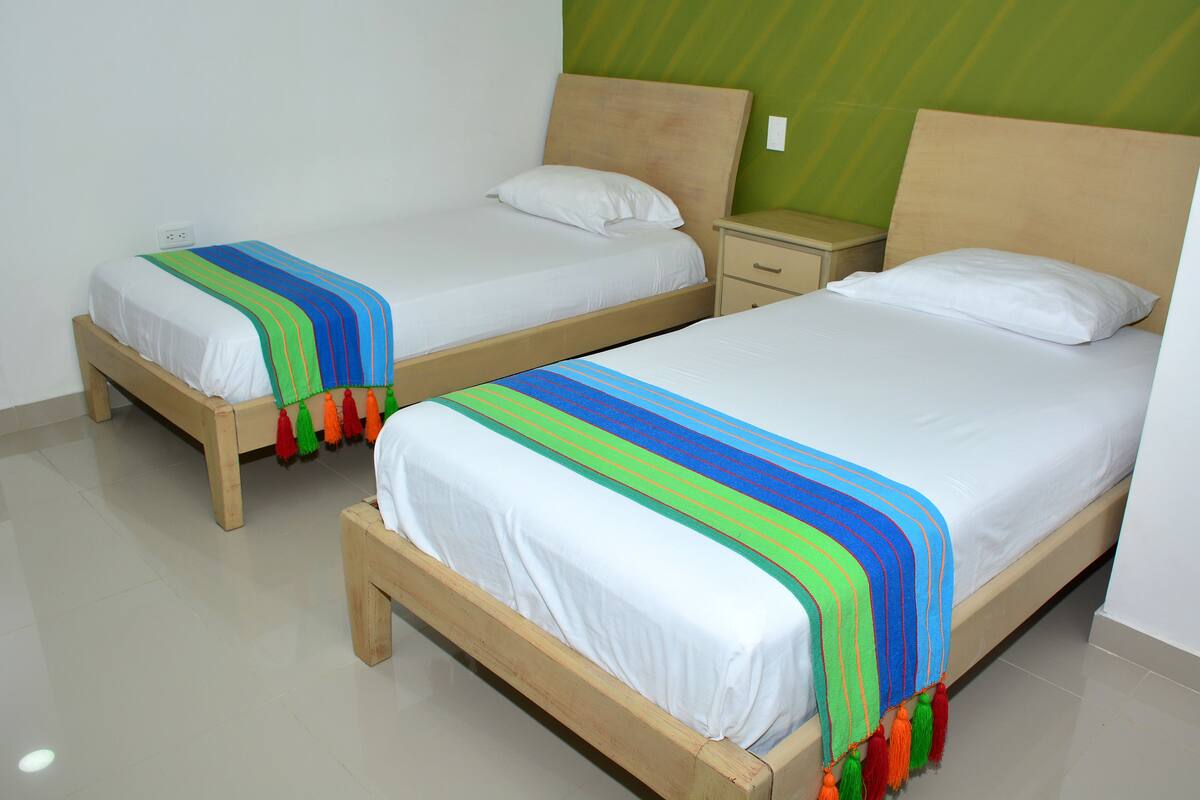 Two single beds with wooden frames and white bedding, a small bedside table, and a green accent wall.