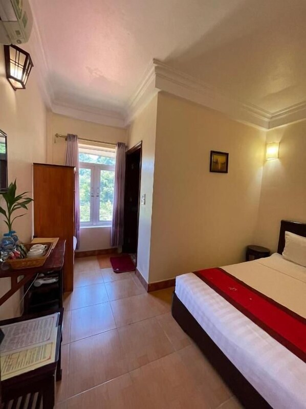 A hotel room with a bed, a desk with a chair, a small table, a potted plant, and a window with curtains. - Chez Loan Hotel (Nam Hoa Lu)