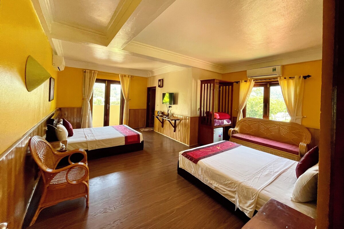 A hotel room with two beds, a sofa, a desk, and an air conditioning unit.