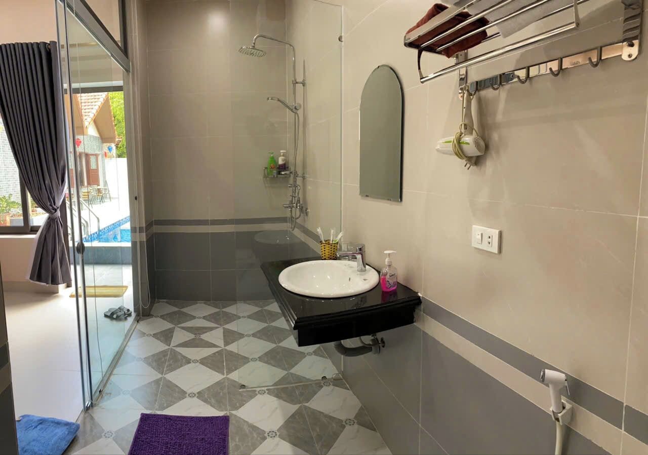 Un baño con mampara de vidrio, un lavabo con encimera negra y un perchero en la pared.