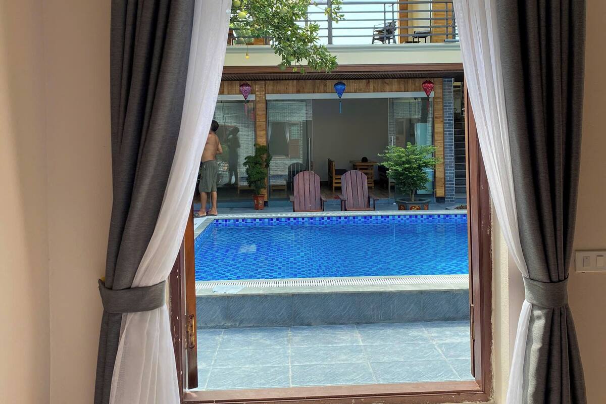 Ein Zimmer mit Fensterblick auf einen Pool, Vorhänge und eine Ansicht eines Gebäudes mit Außenbereich.