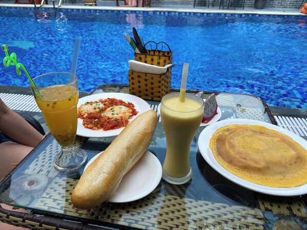 A dining table with a meal consisting of a bread roll, a plate of pasta, a drink with a straw, and a crepe. - Tam Coc Westlake Homestay - Hostel (Hoa Lu)