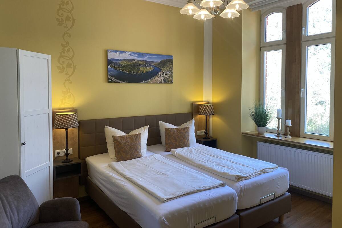 Quarto de hotel com uma cama grande, duas luminárias de cabeceira, um quadro na parede e uma janela com vista.