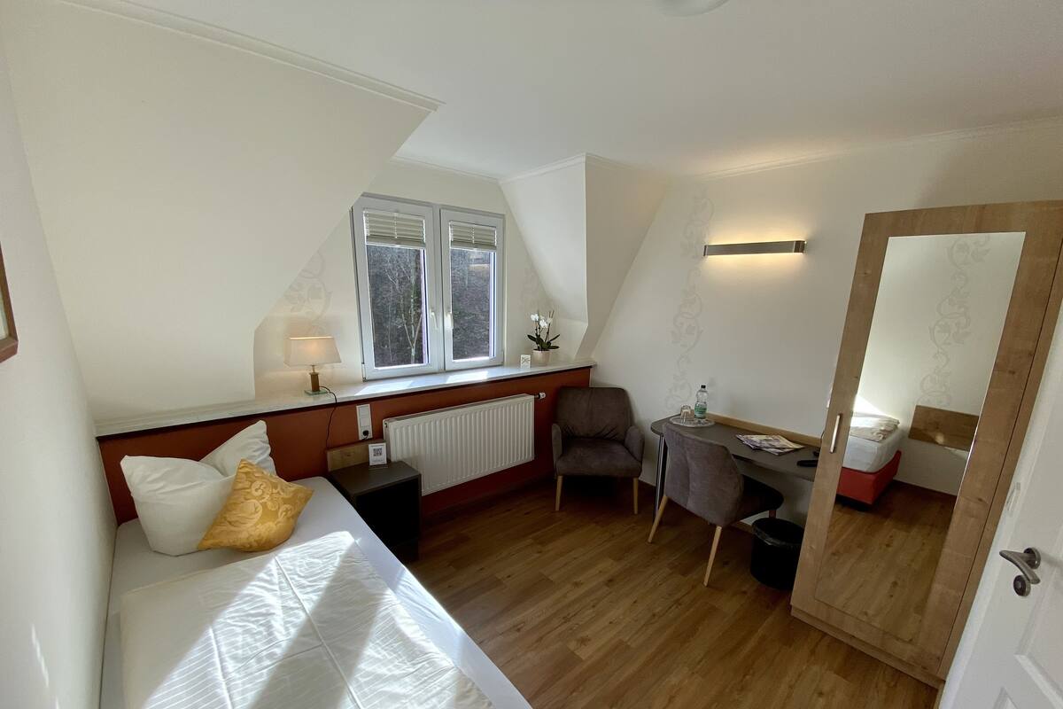 Quarto pequeno com cama, escrivaninha, cadeira e radiador.