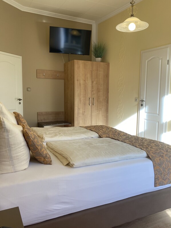 Un dormitorio con cama, televisor montado en la pared y armario de madera.