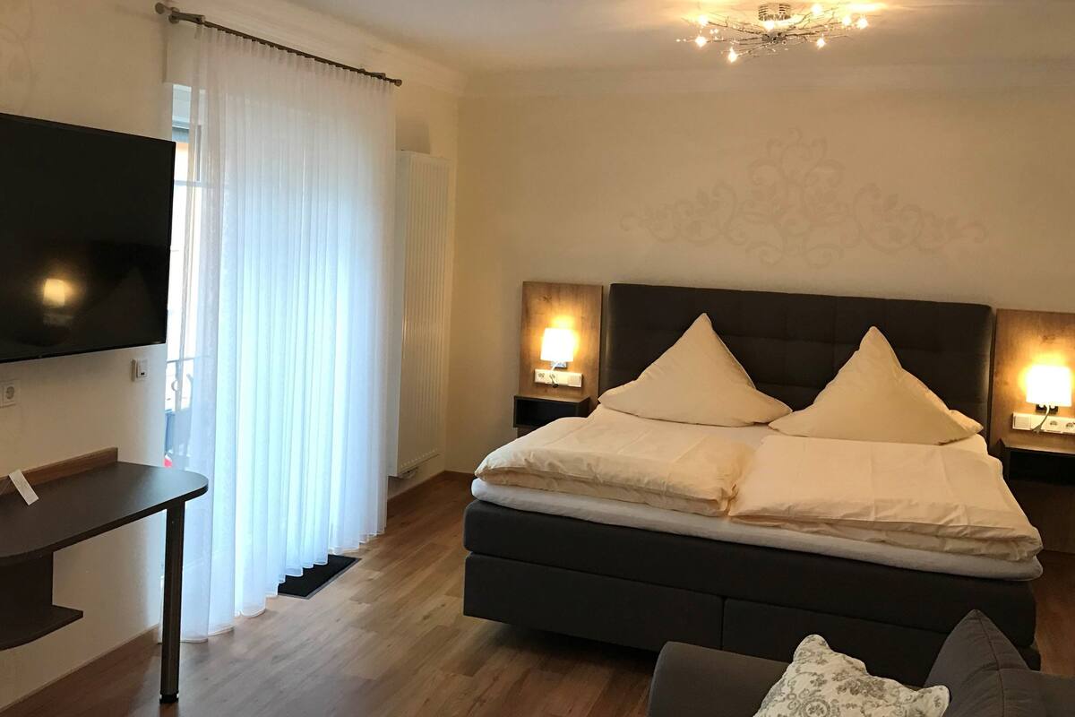 Quarto com cama, abajures, televisão e sofá.