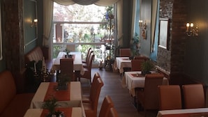 A restaurant with multiple tables and chairs, a chandelier, and a view of the outdoors. - Haus Hohenzollern (Bad Bertrich)