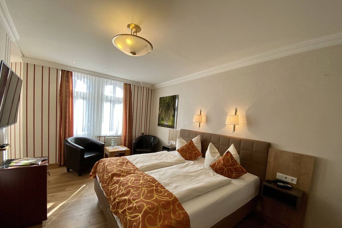 Quarto de hotel com uma cama grande, uma escrivaninha, uma cadeira e uma televisão.