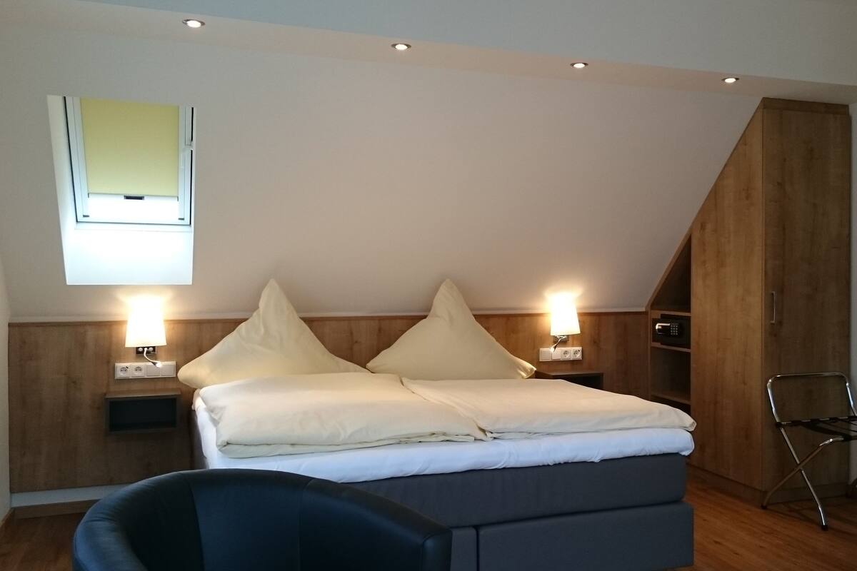 Quarto com cama, duas mesas de cabeceira com luminárias, uma janela, um guarda-roupa de madeira e uma cadeira.