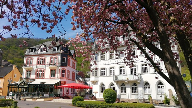 A traditional European building with a red and white facade, surrounded by lush greenery and cherry blossoms. - Haus Hohenzollern (Bad Bertrich)