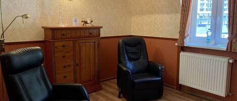 Una habitación con dos sillones de cuero negro, un armario de madera, una lámpara de pared y un ventanal con cortinas.
