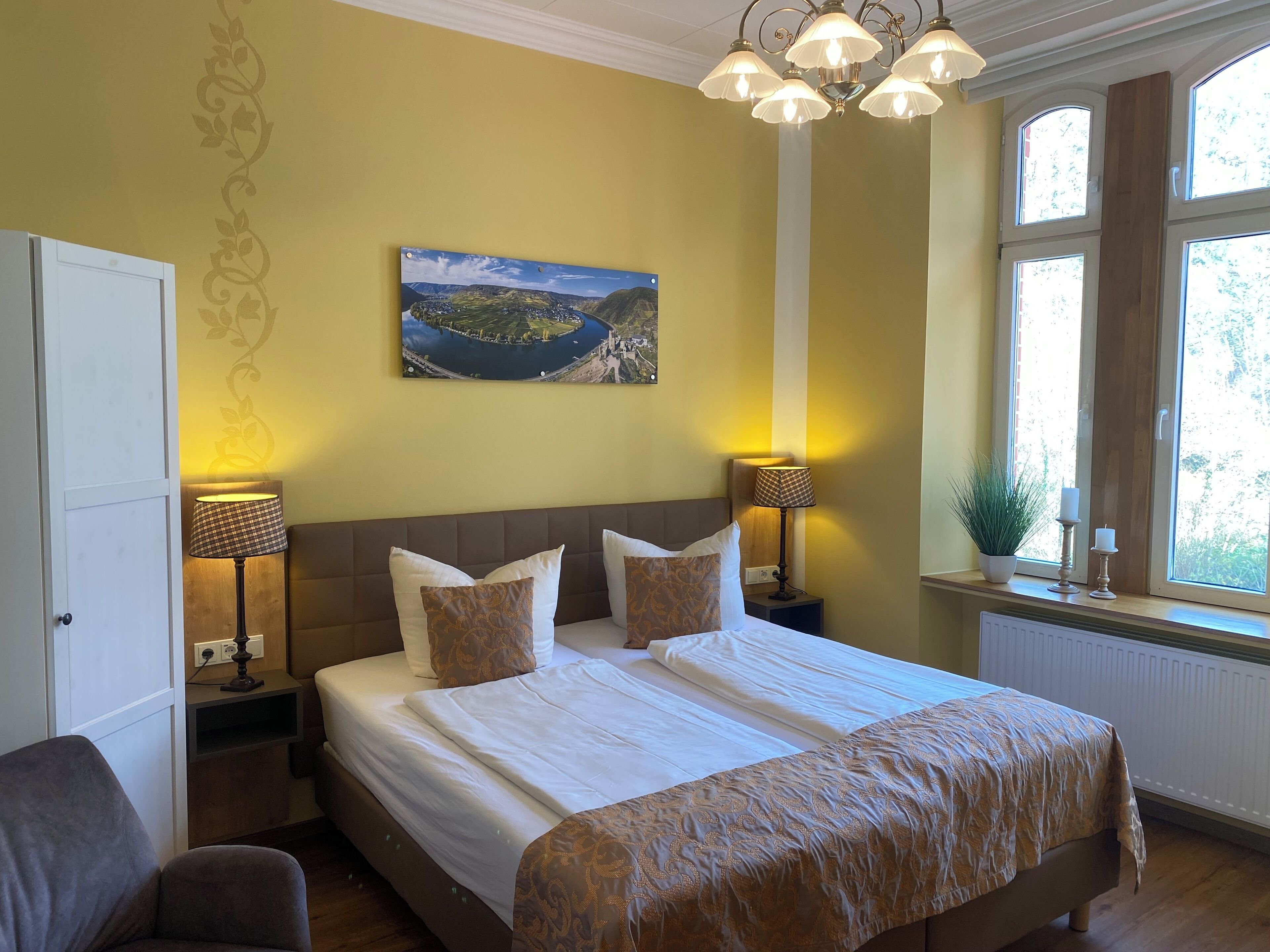 A bedroom with a large bed, two bedside lamps, a painting on the wall, and a window with a view.
