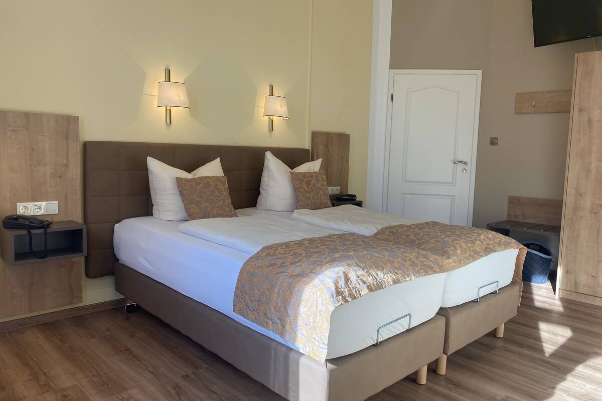 Uma cama de casal com colcha estampada, mesa de cabeceira com telefone e televisão fixada na parede.