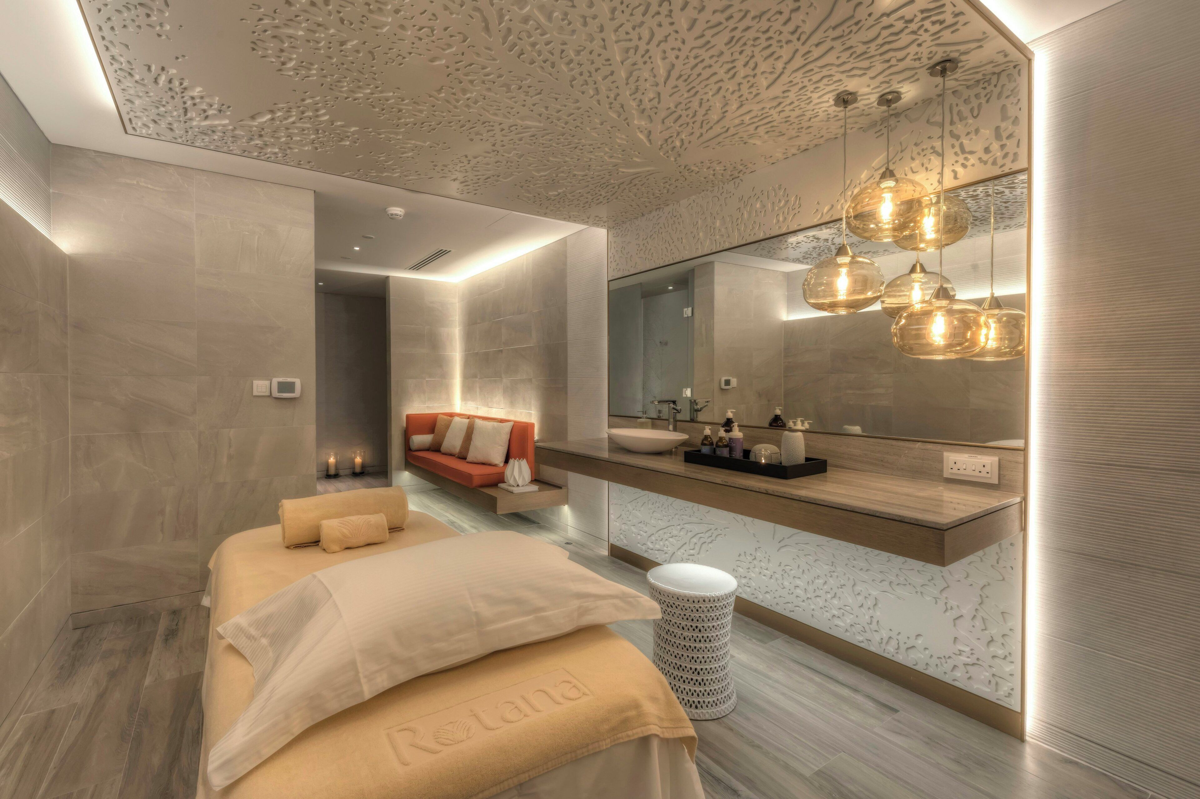 A modern bedroom with a large bed, a sofa, a vanity with a mirror, and pendant lighting.