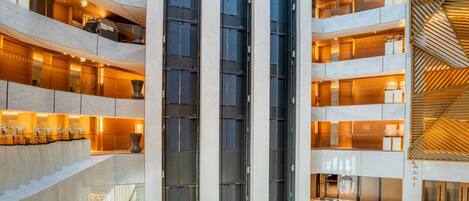 A multi-level atrium with glass railings, a central elevator shaft, and a modern design with geometric patterns.