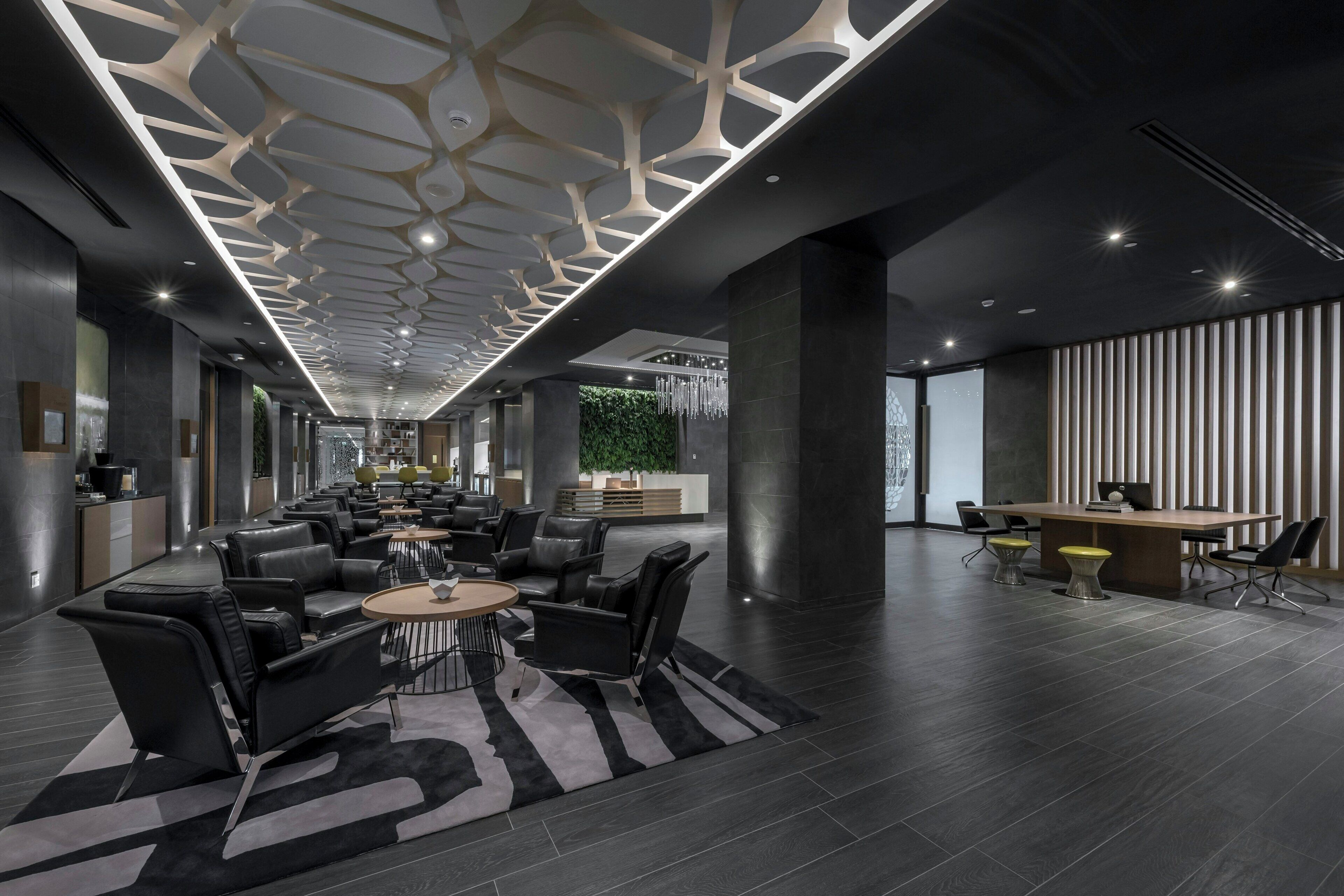 Un hall d’hôtel moderne avec un espace salon central, un comptoir d’accueil et un mur végétal.