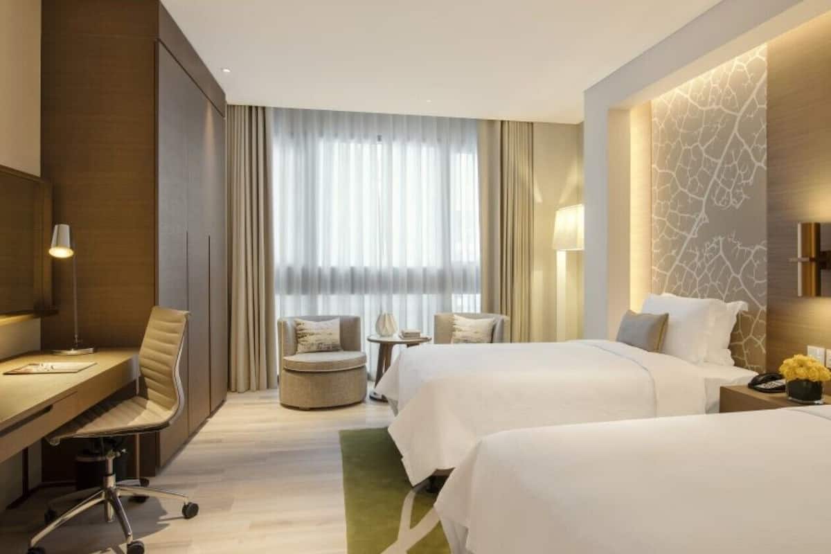 Une chambre d’hôtel avec deux lits, un bureau, une chaise, une petite table et une fenêtre avec des rideaux.