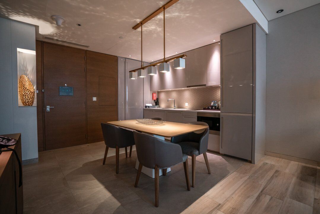 A modern kitchen with a dining area, featuring a wooden table, chairs, and pendant lights.
