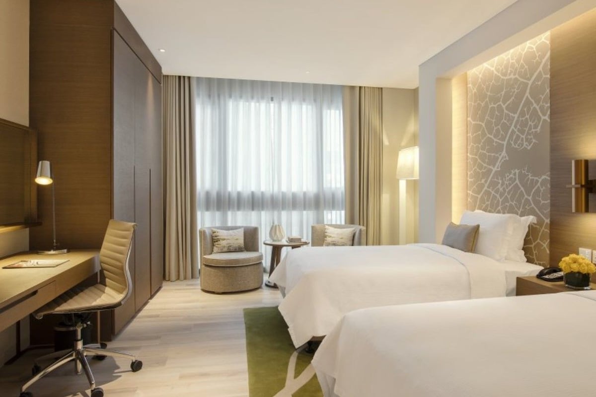 Habitación de hotel con dos camas, un escritorio, una silla, una mesita y una ventana con cortinas.