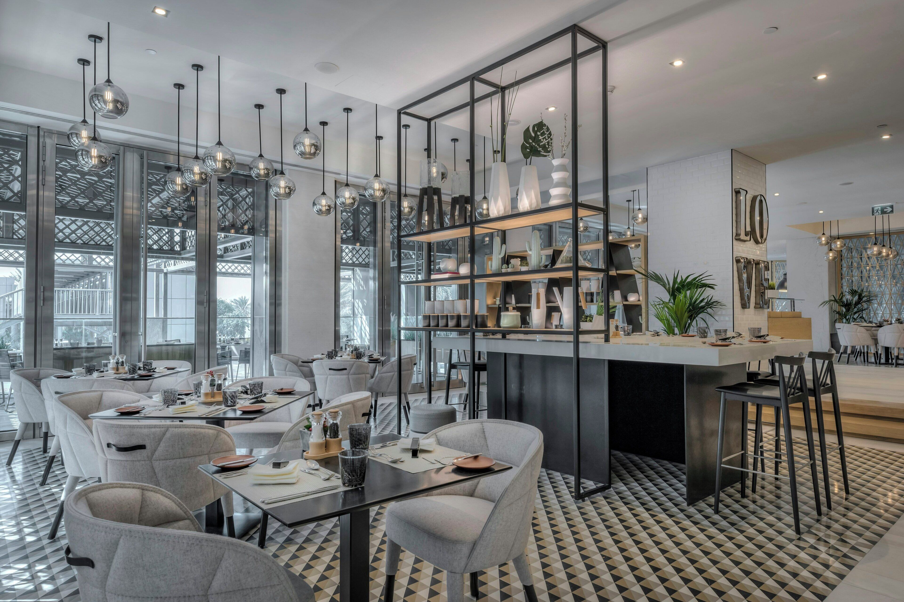 A modern dining area with multiple tables, chairs, and hanging pendant lights.