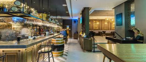 Eine moderne Bar mit einer langen Theke, Hockern und einer Auswahl an Flaschen und Gläsern.