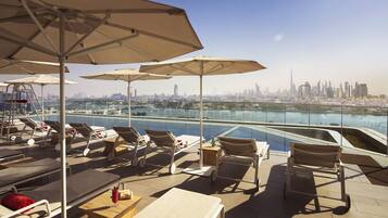 A rooftop terrace with lounge chairs, umbrellas, and a view of a city skyline and water body.