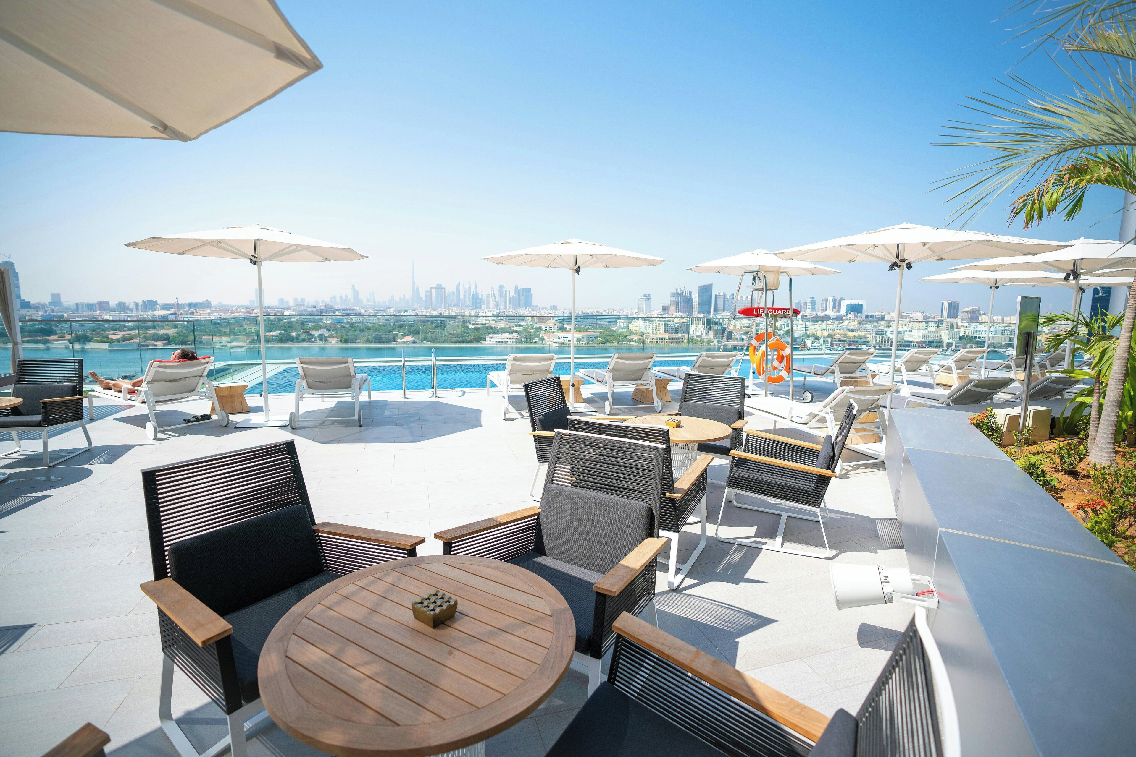 A rooftop bar with outdoor seating, umbrellas, and a pool view.