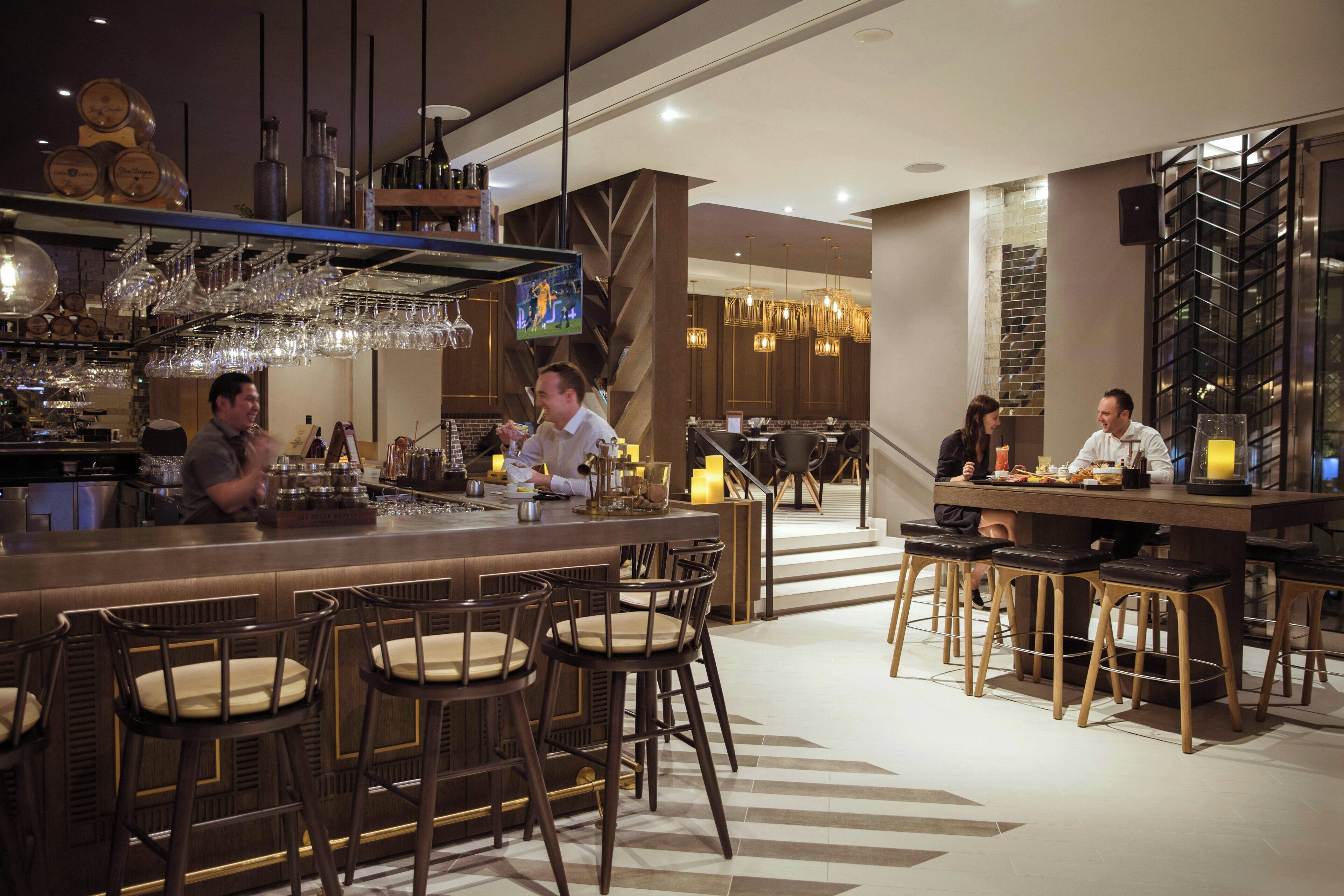 A bar area with stools, a television screen, and a variety of bottles and glasses.
