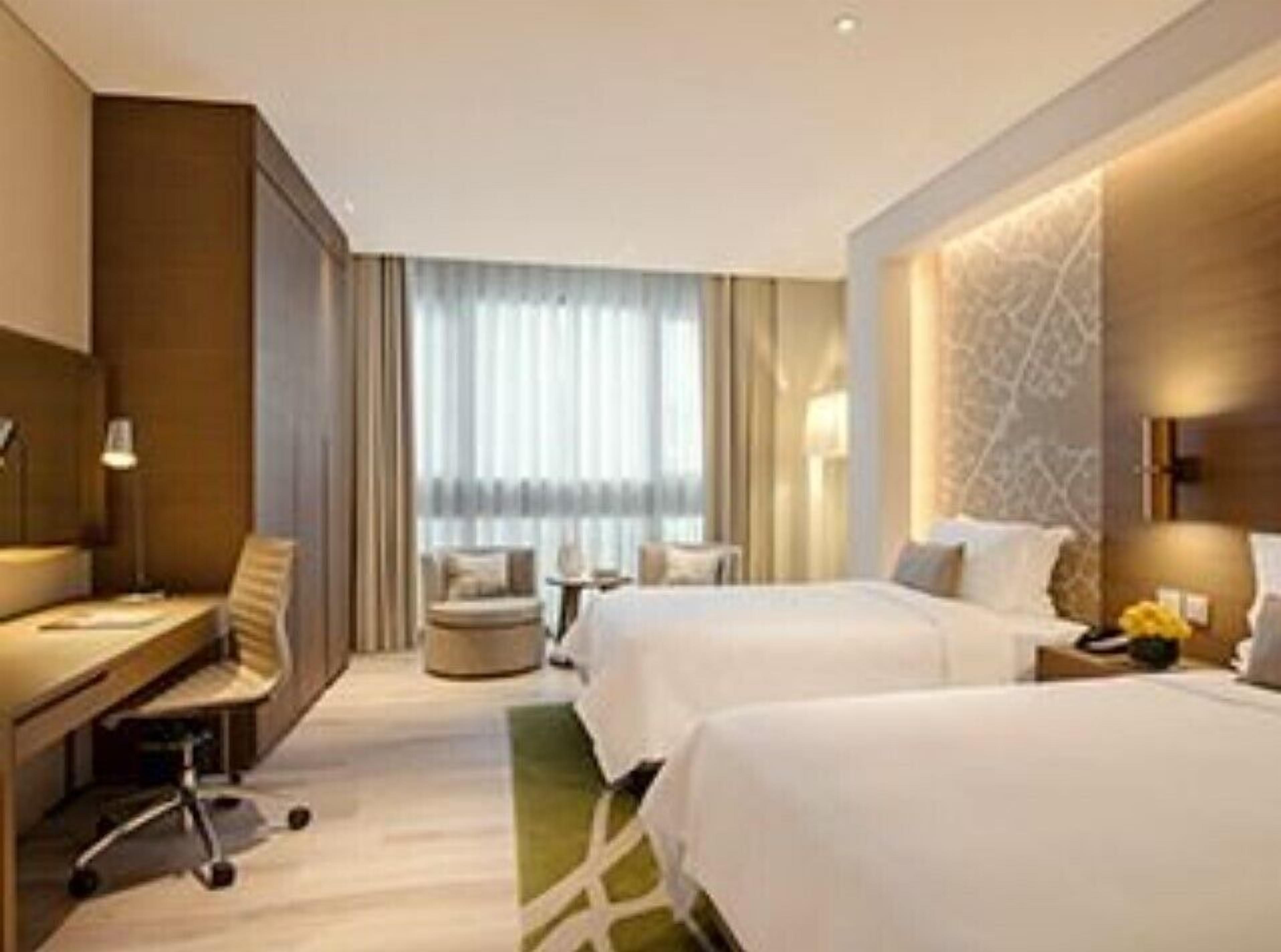 A hotel room with two beds, a desk, a chair, and a view of the outdoors.