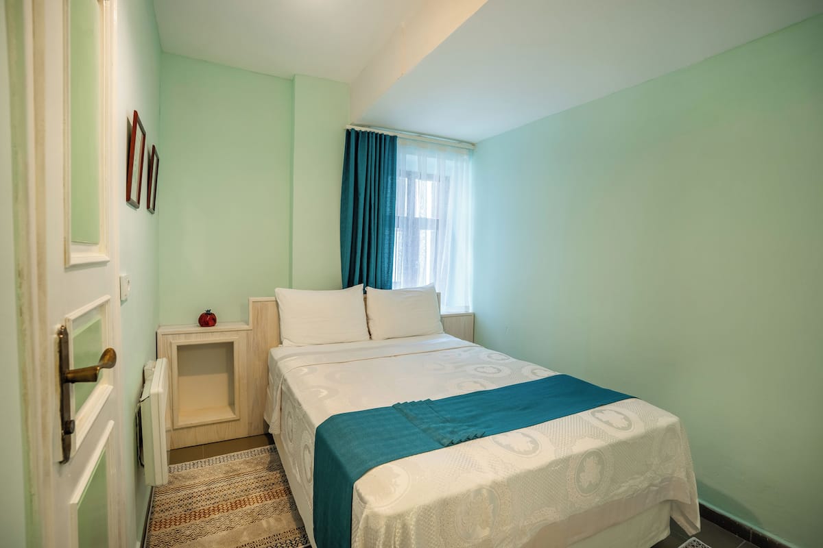 A bedroom with a bed, a nightstand, a window with curtains, and a door.