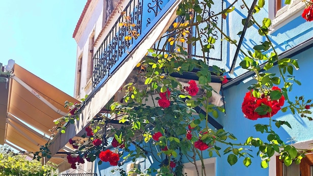 Un bâtiment bleu doté d’un balcon, de sièges en plein air et de plantes en pot.