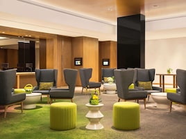 A hotel lobby with grey armchairs, green ottomans, and a reception desk.