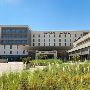 A modern hotel building with a flat roof and a sign that reads "NOVOTEL" in English and another language.