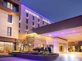 A hotel with a modern facade, a prominent sign reading 'NOVOTEL,' and a well-lit entrance area with a landscaped garden.