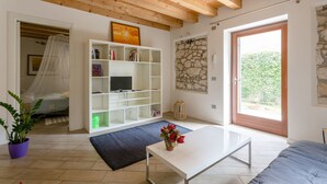A bedroom with a bed, a white TV stand, a stone wall, and a large window.