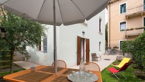 An outdoor patio with a table set for four, surrounded by chairs, under a large umbrella.