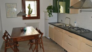 A kitchen with a wooden table, chairs, a window with a cactus, a sink, and a stove.