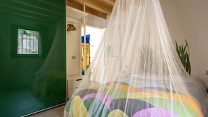 A room with a bed covered in a colorful quilt, a green door, and a wooden ceiling.