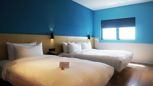 Hotellihuone, jossa on kaksi sänkyä, yöpöytä, seinään kiinnitetty valaisin ja ikkuna.