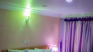 Une chambre d’hôtel avec un lit simple, une table de chevet, une lampe et un rideau.