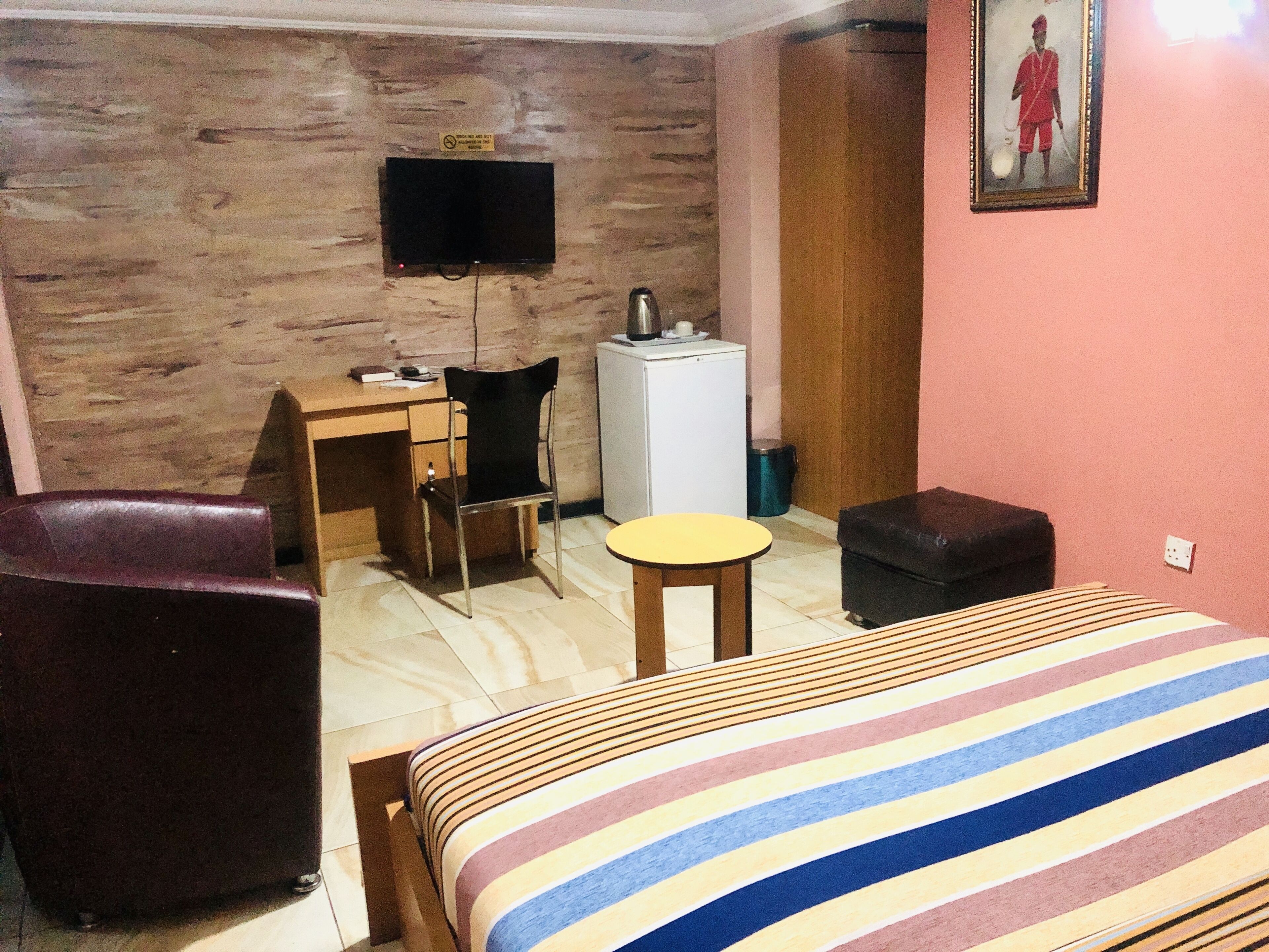 Hotelkamer met een bed, een bureau, een stoel, een tafeltje, een aan de muur bevestigde televisie en een koelkast.
