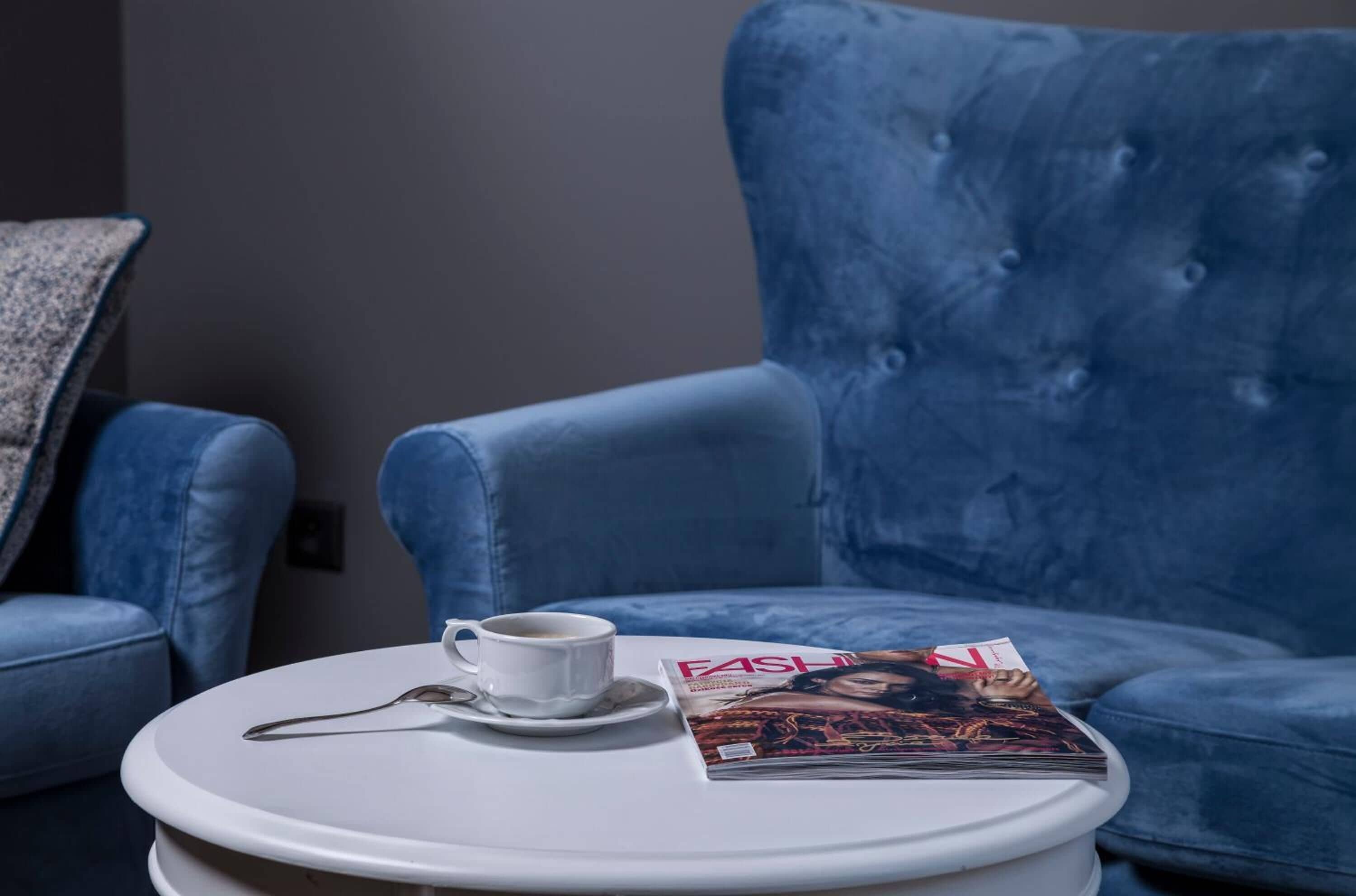 Ein blauer Sessel, ein weißer Beistelltisch mit einer Tasse und einer Zeitschrift.
