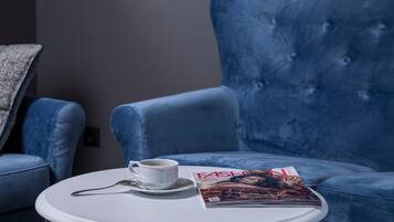 Ein blauer Sessel, ein weißer Beistelltisch mit einer Tasse und einer Zeitschrift.