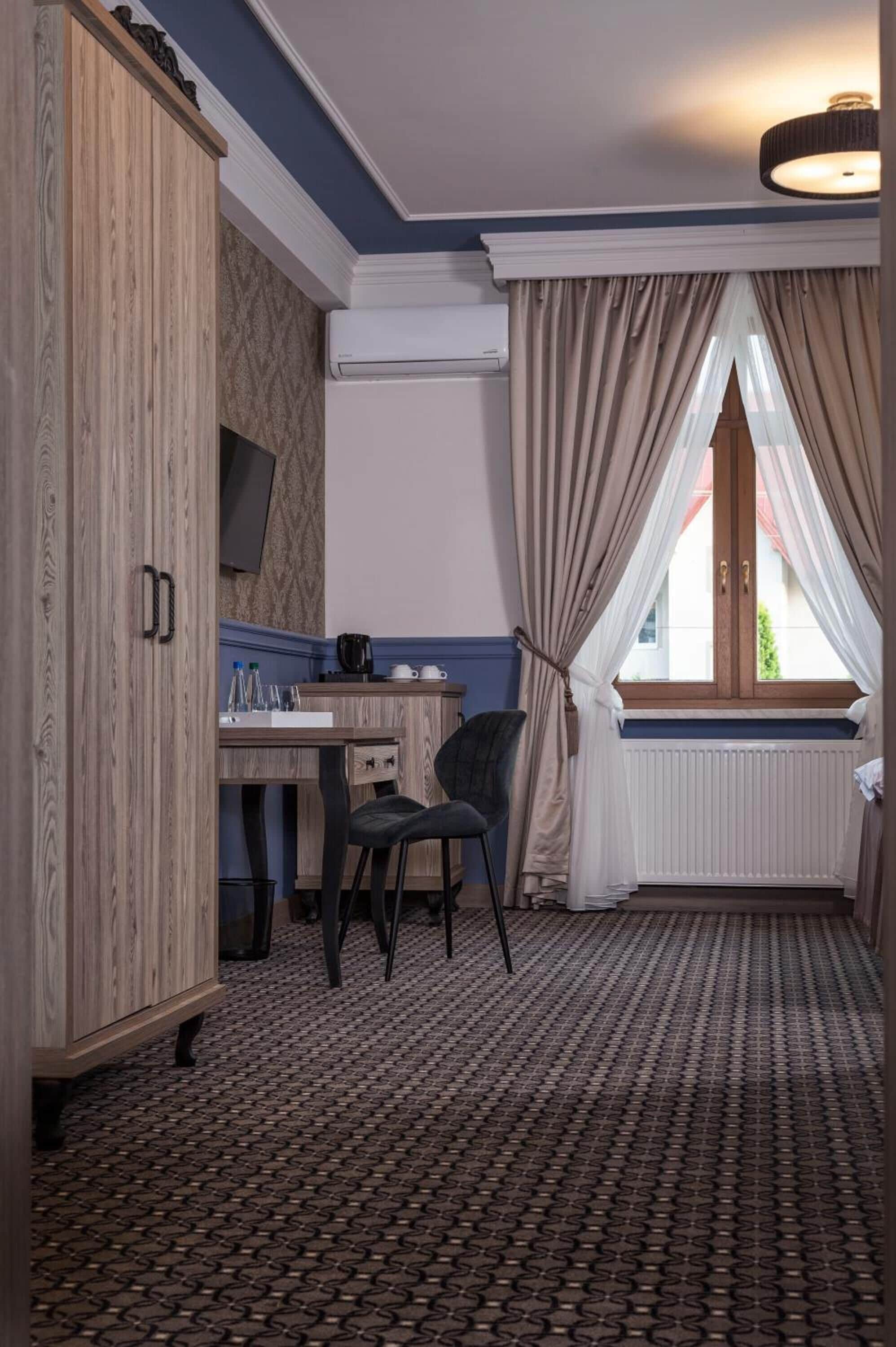 A room with a wooden wardrobe, a desk with a chair, a television, and a window with curtains.
