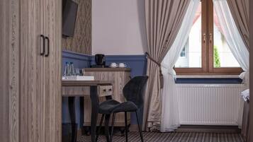 A room with a wooden wardrobe, a desk with a chair, a television, and a window with curtains.