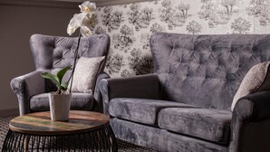 A grey tufted sofa and armchair set with a patterned wallpaper background. - Willa w Dolinie (Tarnow)