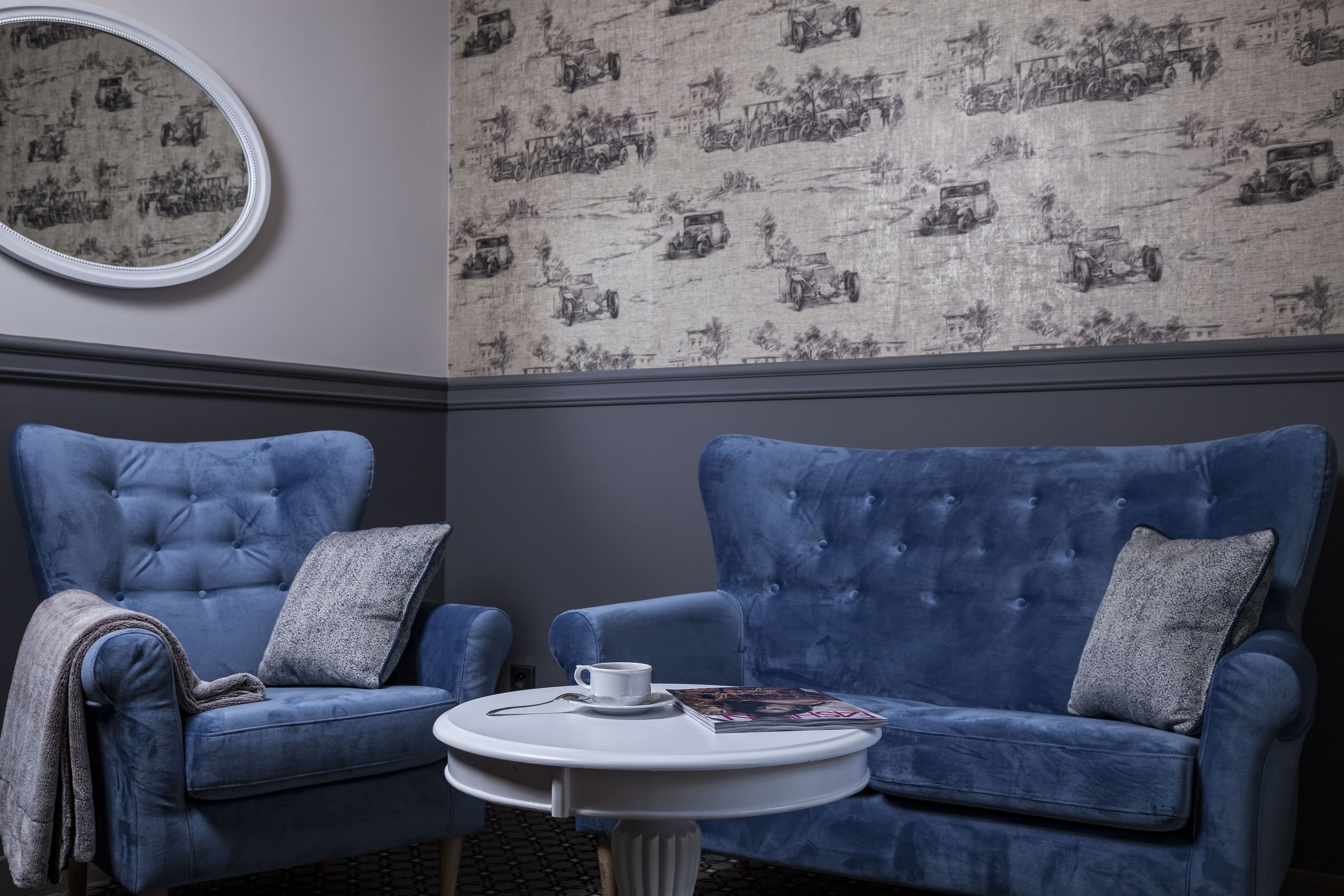 A room with a blue sofa, a round white table, and a patterned wallpaper.