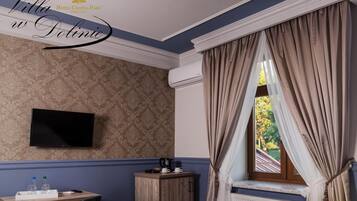 A hotel room with a patterned wallpaper, a flat-screen TV, a wooden cabinet, a window with curtains, and a radiator.