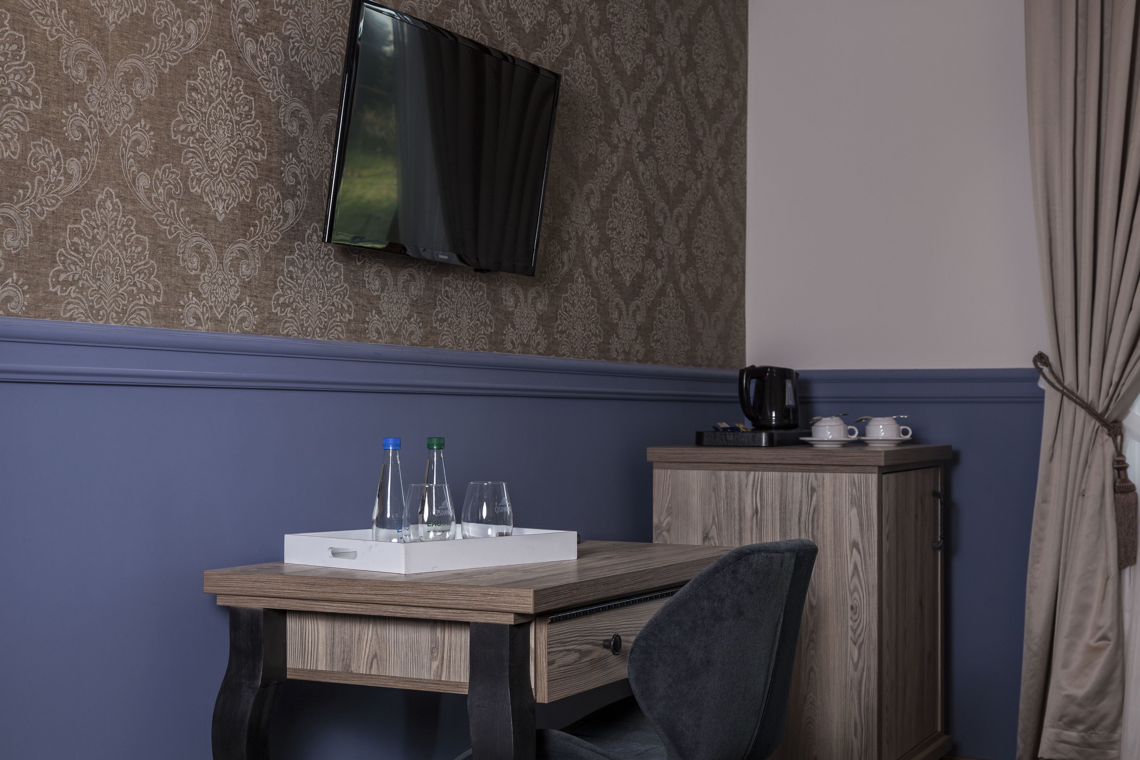 Een kamer met een houten bureau, een aan de muur bevestigde televisie, een kast en een stoel.