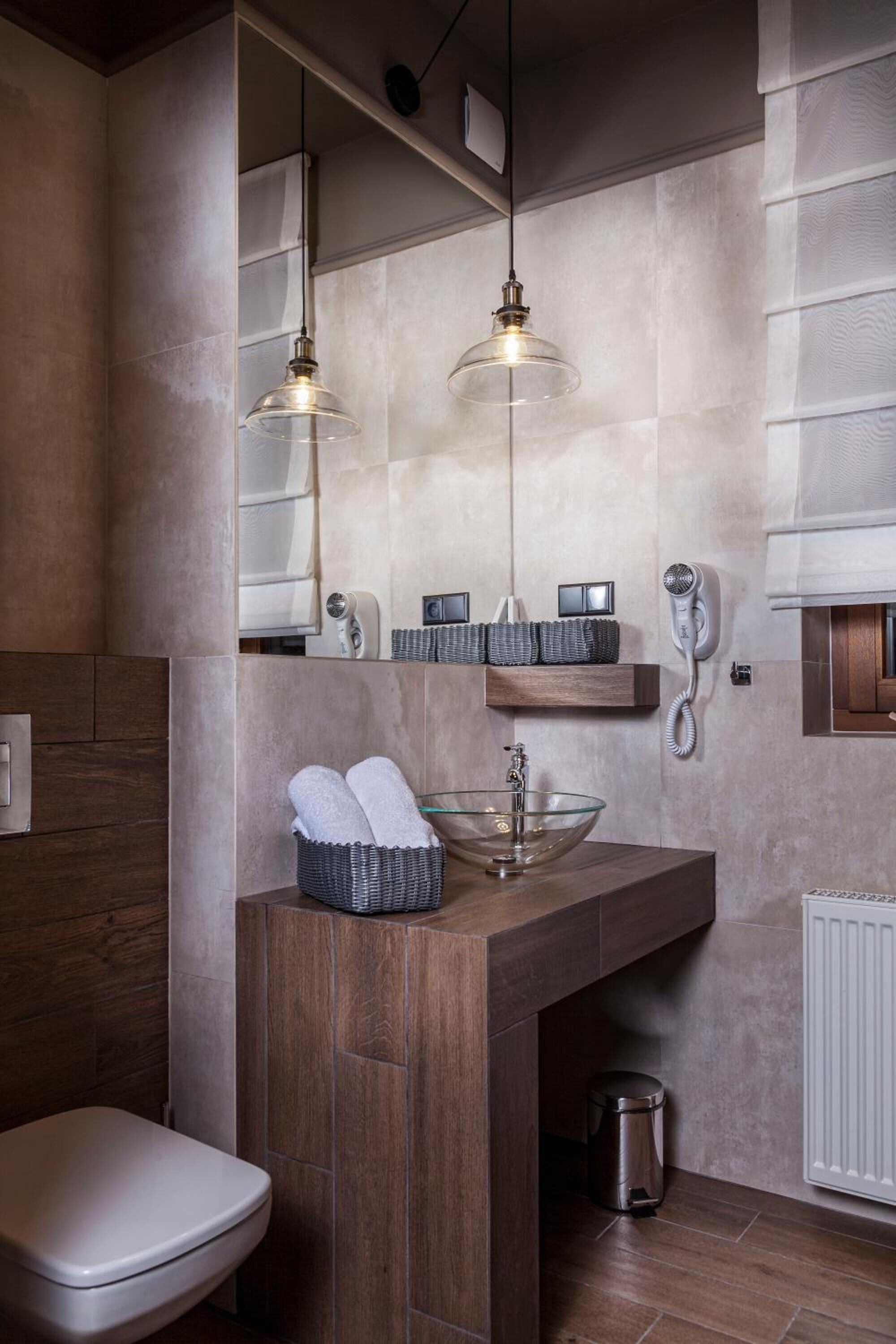 A modern bathroom with a wooden vanity, a glass bowl sink, and two pendant lights.